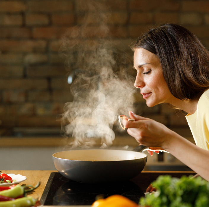 Mulher experimentando comida de uma panela sobre o fogão